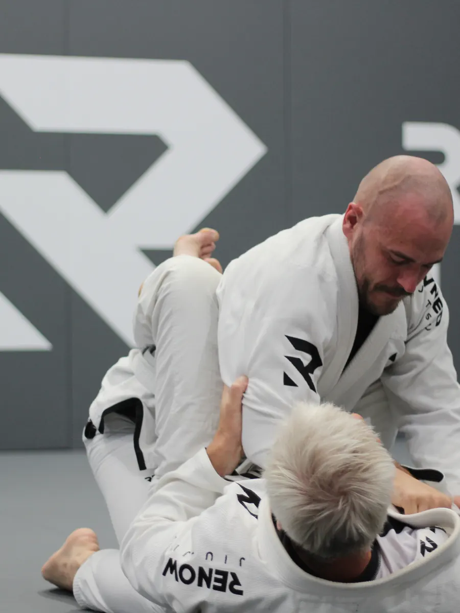 A coach kneeling on the mat, walking a student through a position